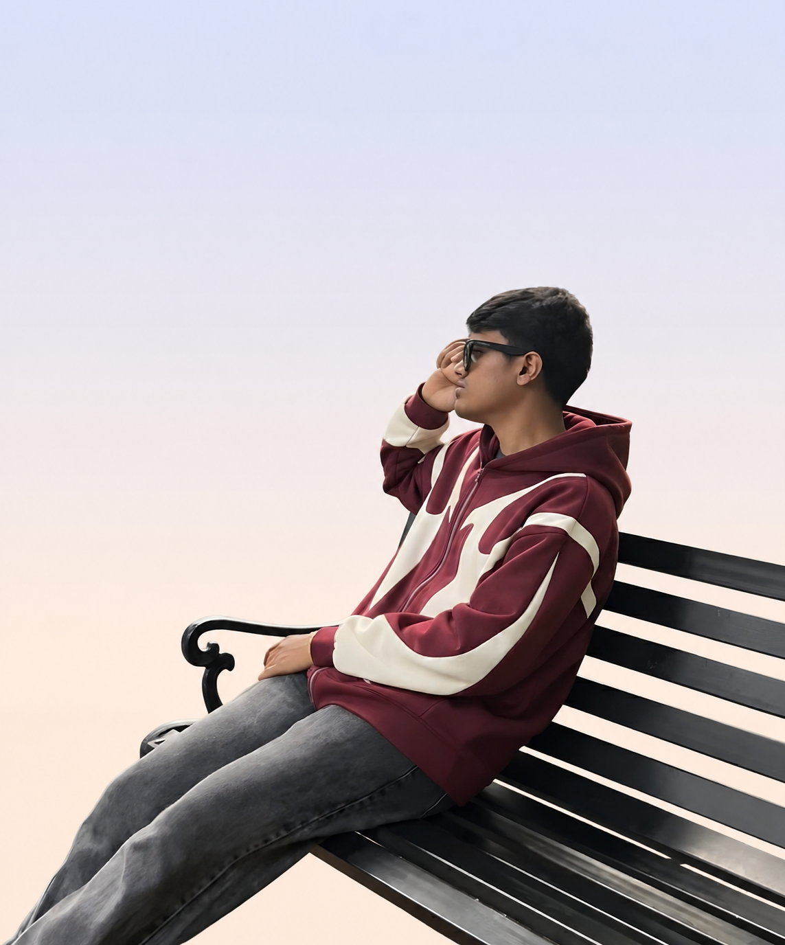 Abrar Ayman seated on a black bench against a light blue-to-peach gradient