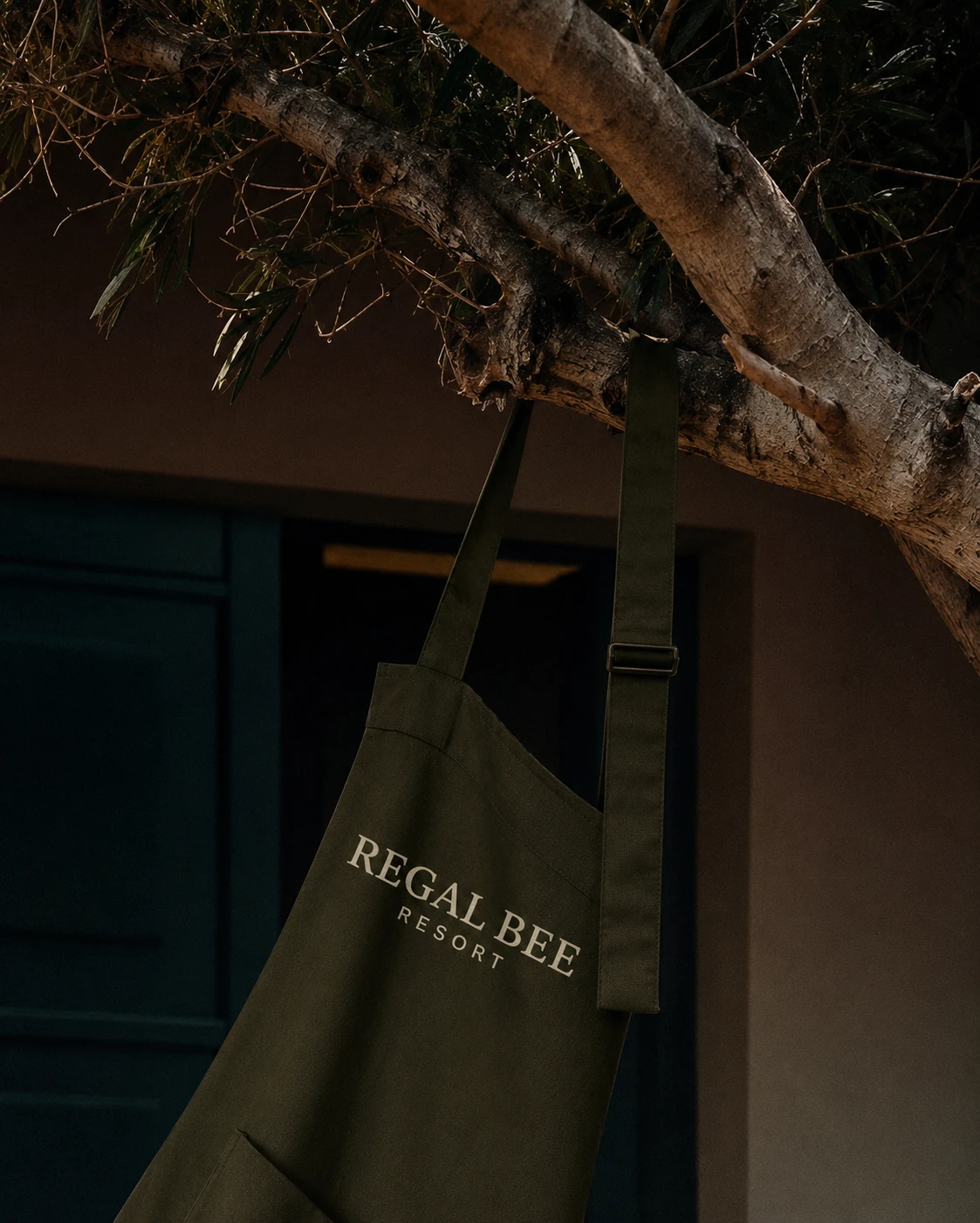 Regal Bee Resort logo printed on a dark green hospitality apron hanging from a tree
